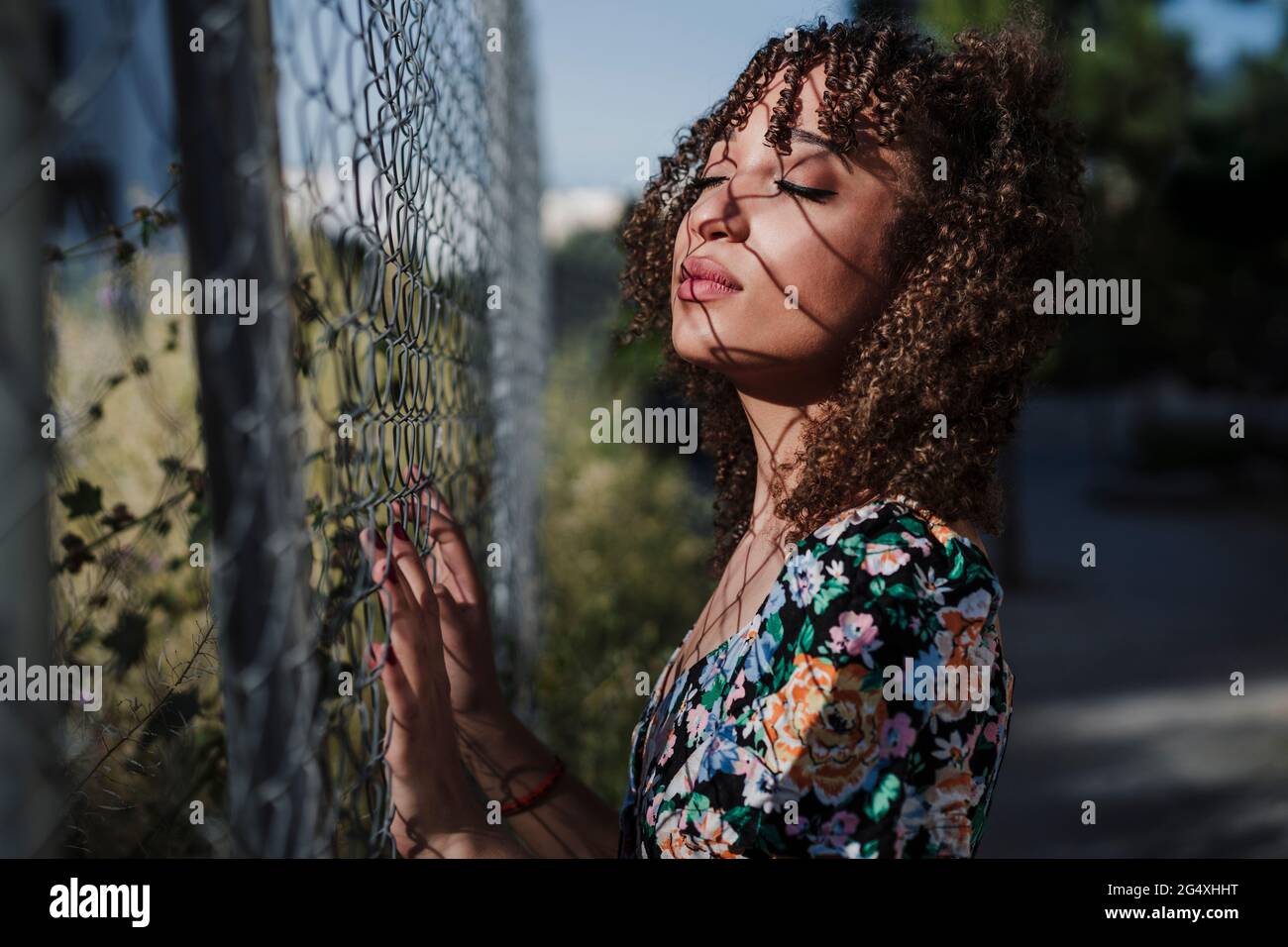 Belle femme debout avec les yeux fermés par la clôture Banque D'Images