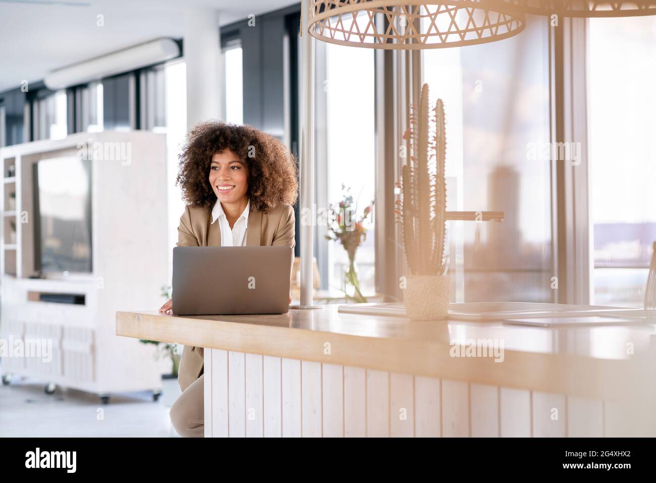 Femme d'affaires souriante contemplant tout en se tenant devant un ordinateur portable à la cafétéria du bureau Banque D'Images