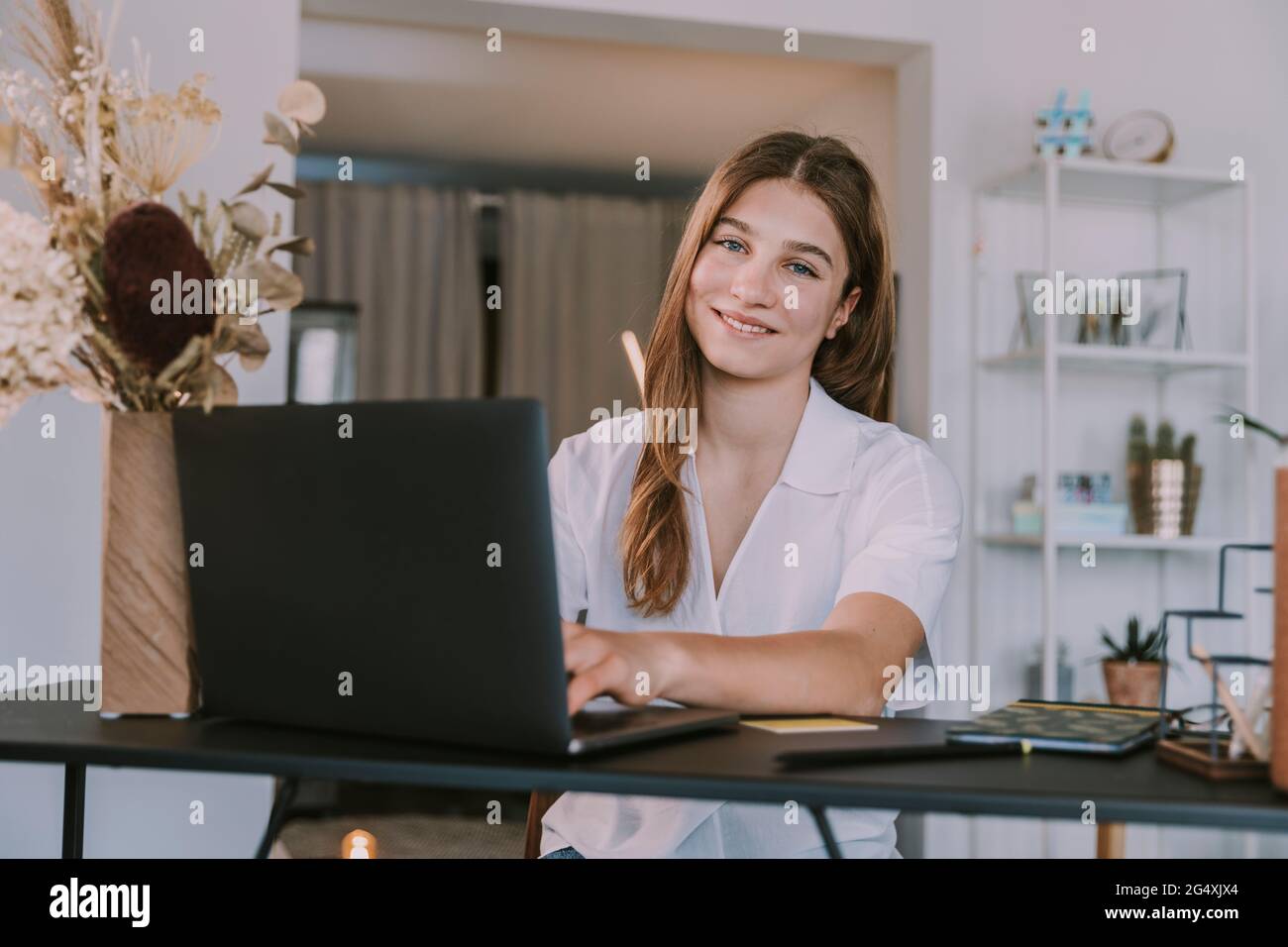 Femme souriante étudiant utilisant un ordinateur portable sur le bureau à la maison Banque D'Images
