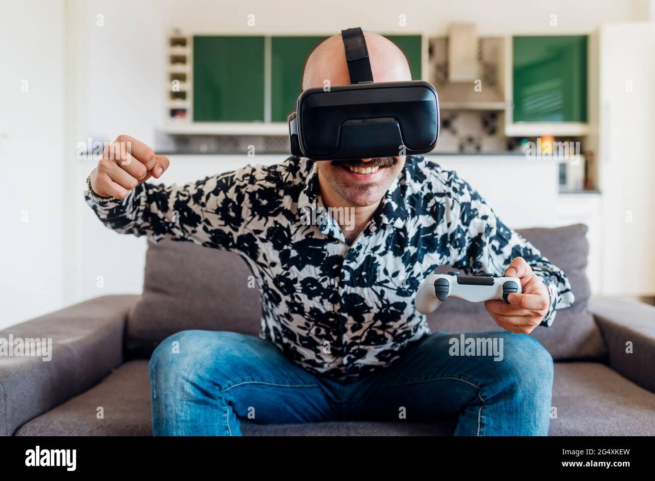 Homme souriant portant un casque de réalité virtuelle qui frappe tout en  tenant la manette de jeu sur le canapé à la maison Photo Stock - Alamy