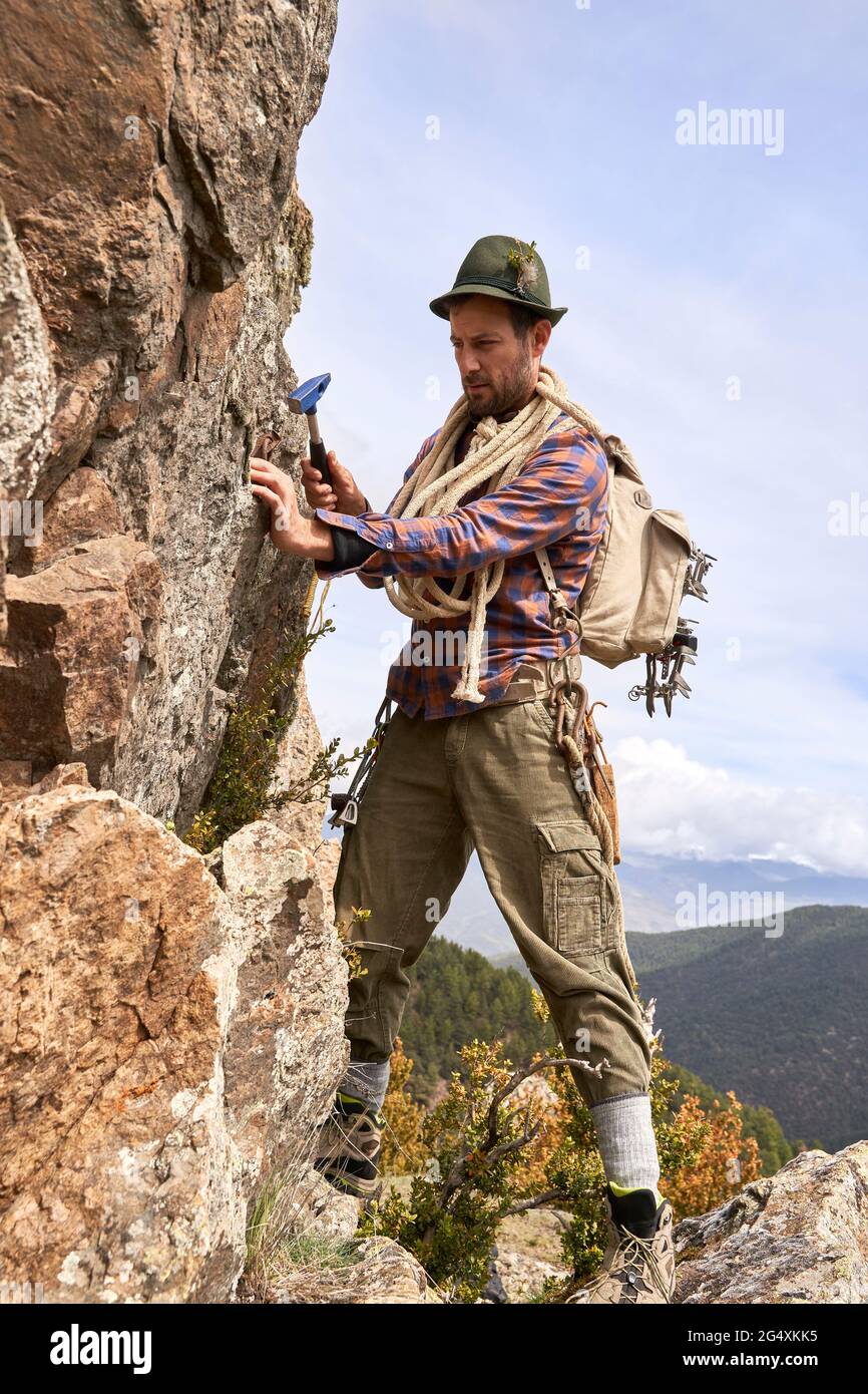 Touriste mâle avec sac à dos et marteau debout au bord du rocher sur la montagne Banque D'Images