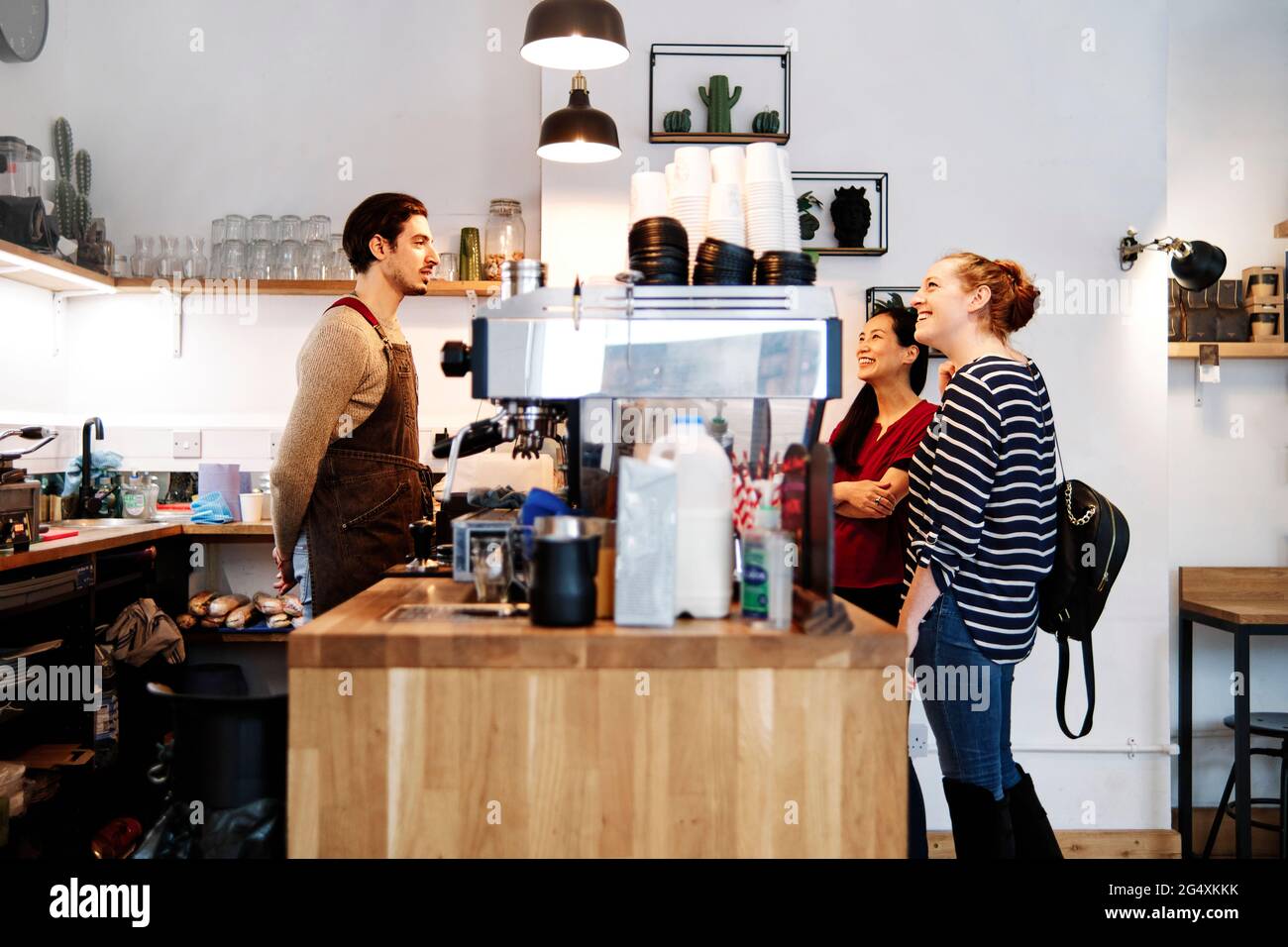 Souriante, les femmes qui regardent la suspension tout en se tenant devant le propriétaire au comptoir du café Banque D'Images