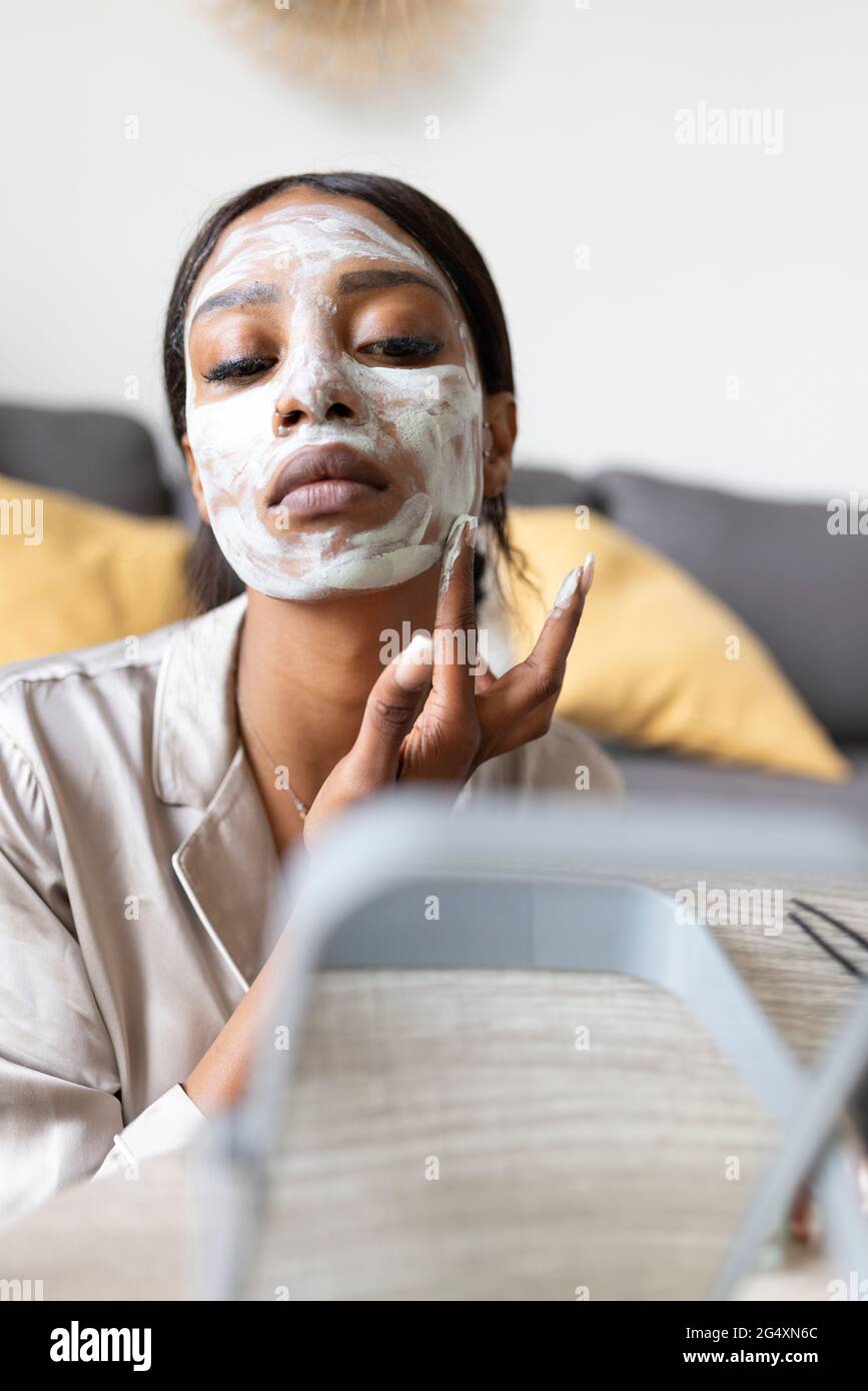 Jeune femme prenant un masque de soin de peau à la maison Banque D'Images