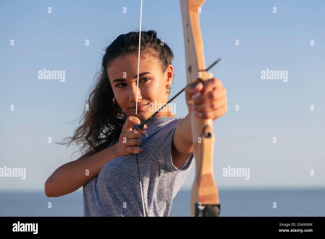 Jeune femme pratiquant le tir à l'arc pendant la journée ensoleillée Banque D'Images