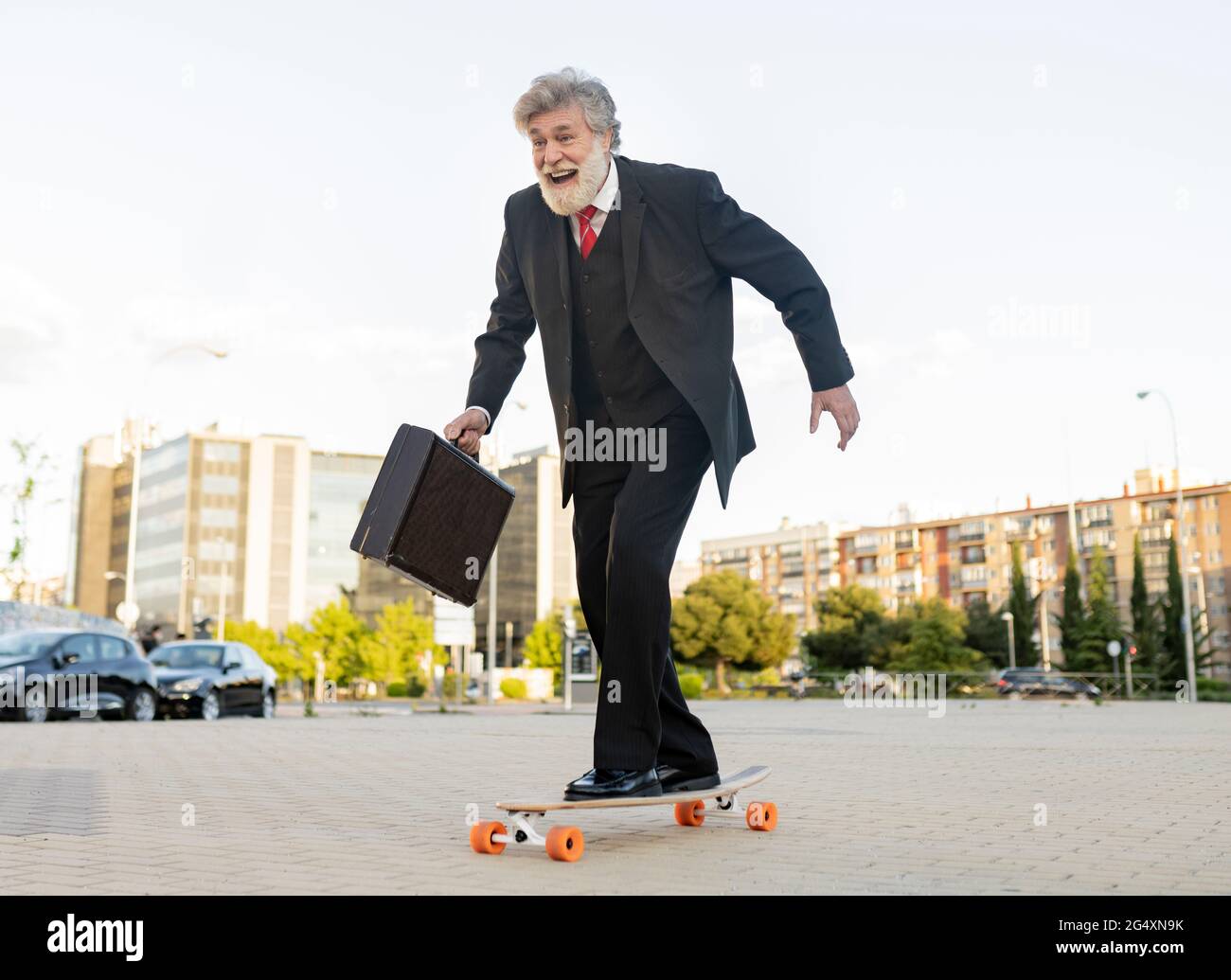 Un homme d'affaires heureux qui se déplace à bord d'un skateboard en ville Banque D'Images