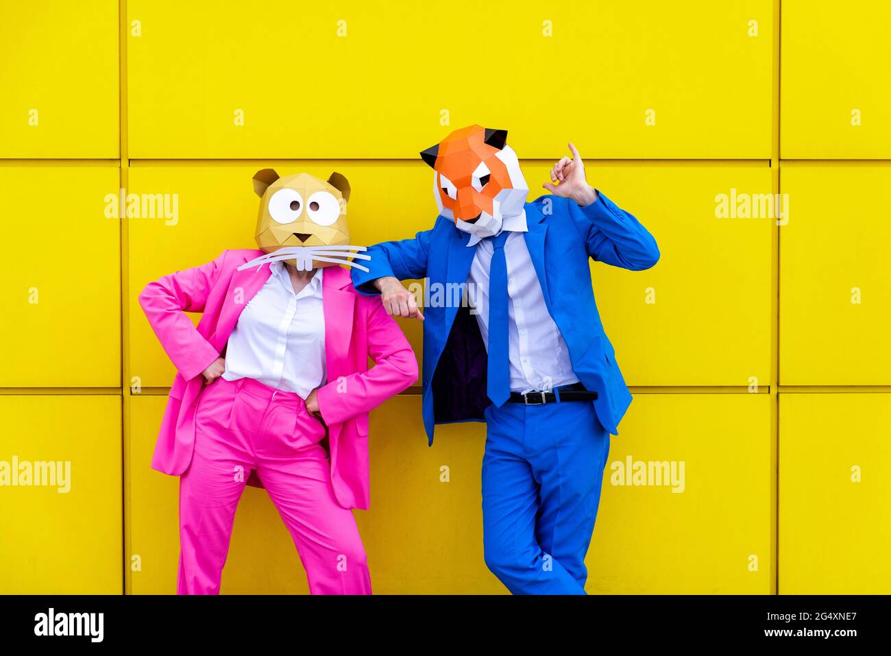 Homme et femme portant des costumes vibrants et des masques pour animaux se posant ensemble contre le mur jaune Banque D'Images