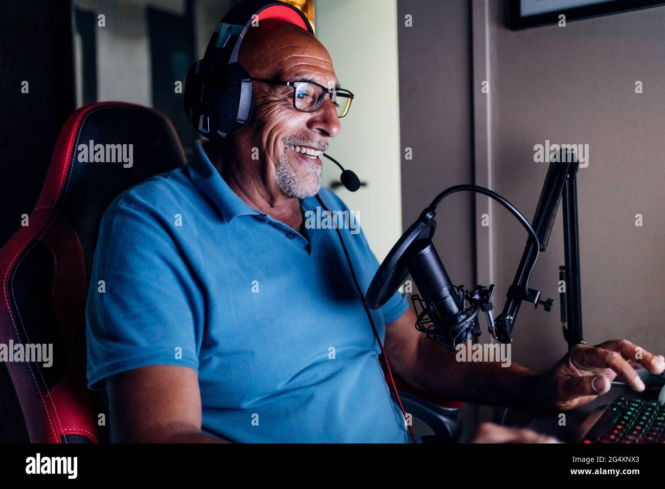 Homme senior souriant portant un casque à l'aide d'un clavier tout en jouant à un jeu vidéo à la maison Banque D'Images