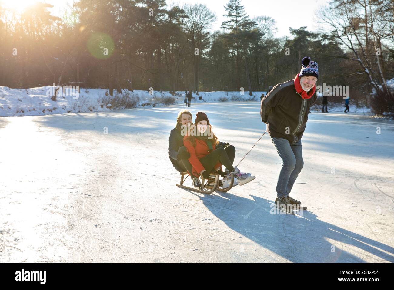 Homme senior patinage sur glace tout en tirant un couple sur un traîneau au-dessus d'un lac gelé Banque D'Images