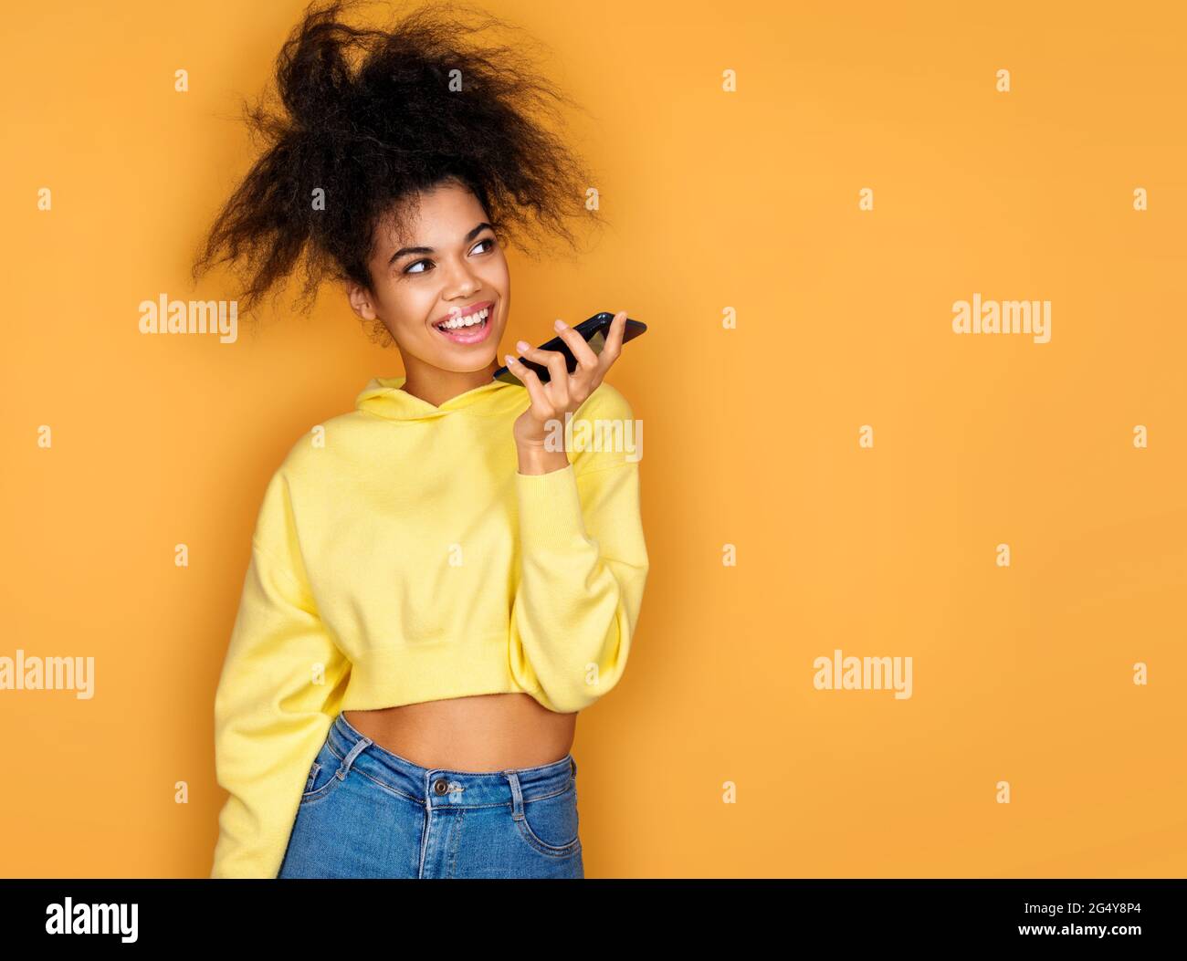 Fille utilise le téléphone, laisse un message vocal. Photo d'une fille afro-américaine sur fond jaune Banque D'Images