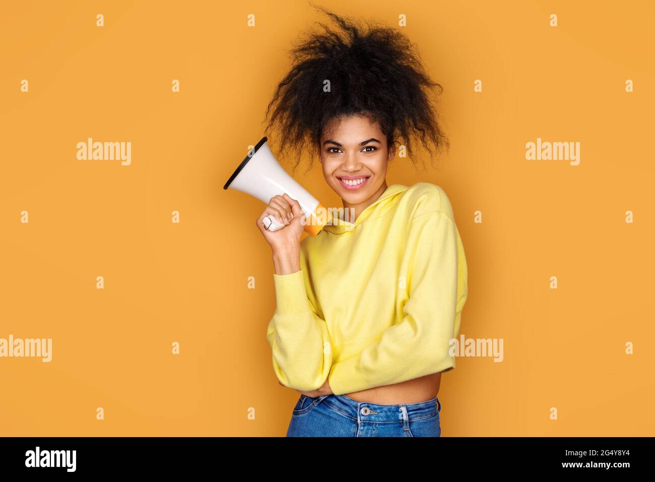 Une fille souriante tient le mégaphone à la main. Photo d'une fille afro-américaine sur fond jaune Banque D'Images
