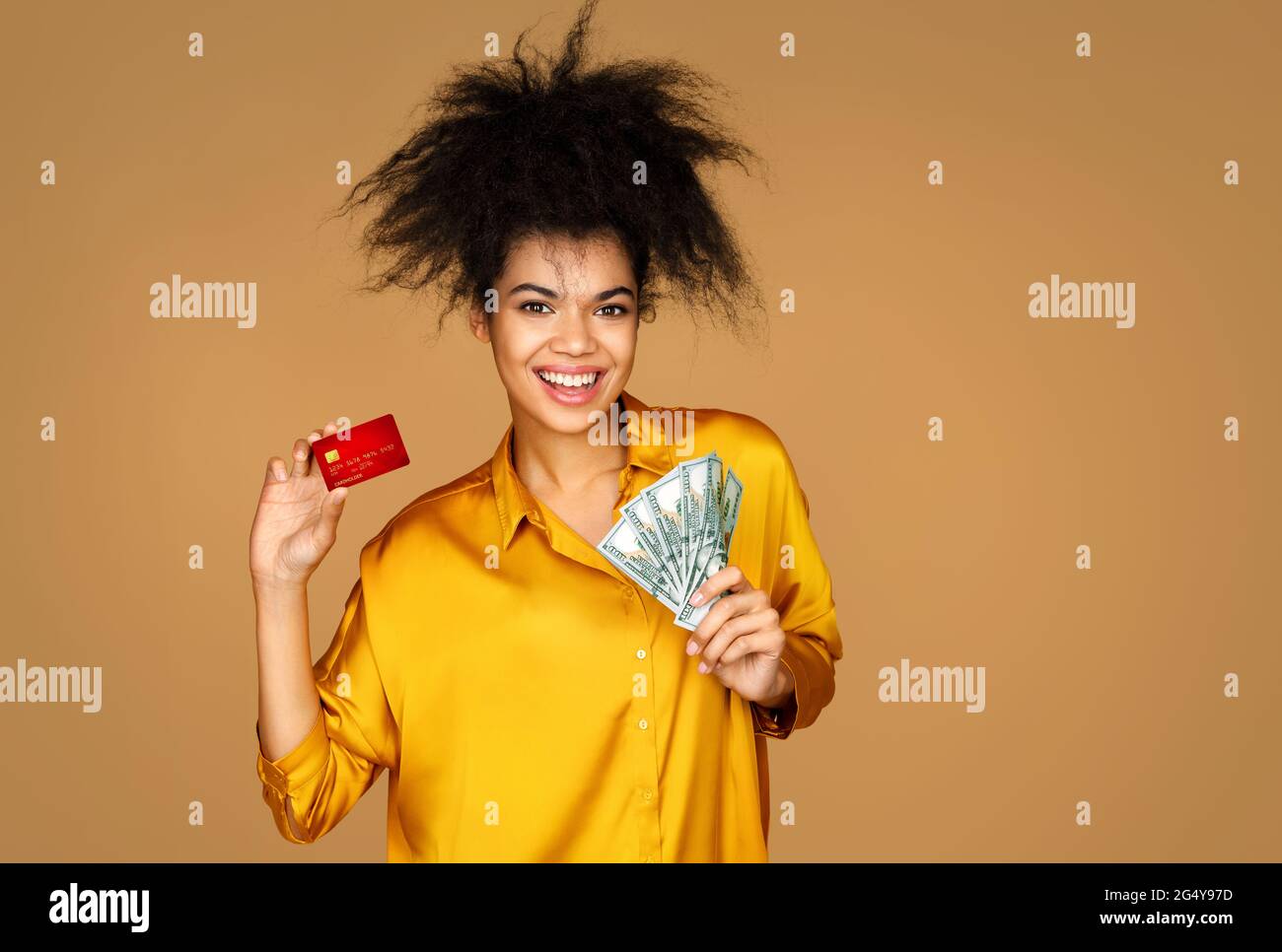 Une fille souriante tient sa carte de crédit et son argent. Photo d'une fille afro-américaine sur fond beige Banque D'Images