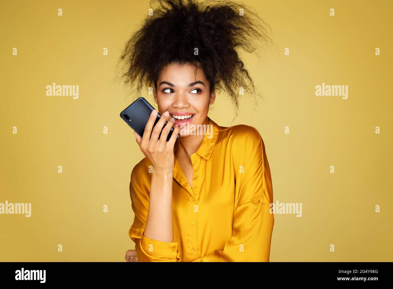 Mignon fille utilise le téléphone, laisse un message vocal. Photo d'une fille afro-américaine sur fond jaune Banque D'Images