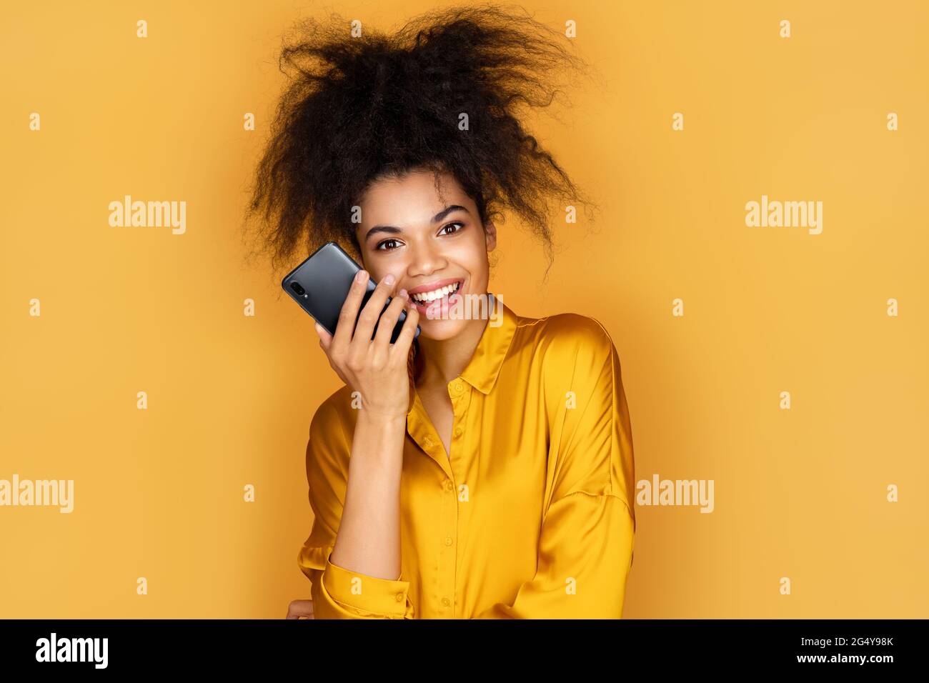 Fille utilise le téléphone, laisse un message vocal. Photo d'une fille afro-américaine sur fond jaune Banque D'Images