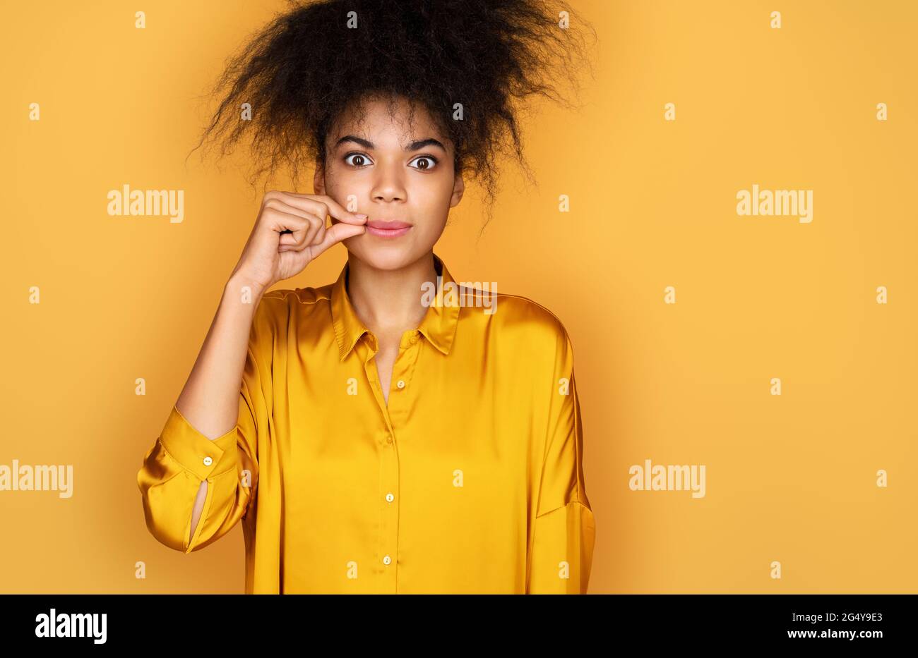Ne dites plus. Elle se ferme la bouche. Photo d'une fille afro-américaine sur fond jaune Banque D'Images