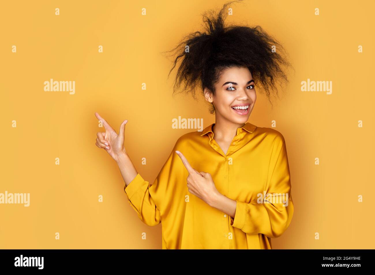 La jeune fille souriante pointe vers l'extérieur avec des index, s'affiche sur l'espace de copie pour votre texte. Photo d'une fille afro-américaine sur fond jaune Banque D'Images