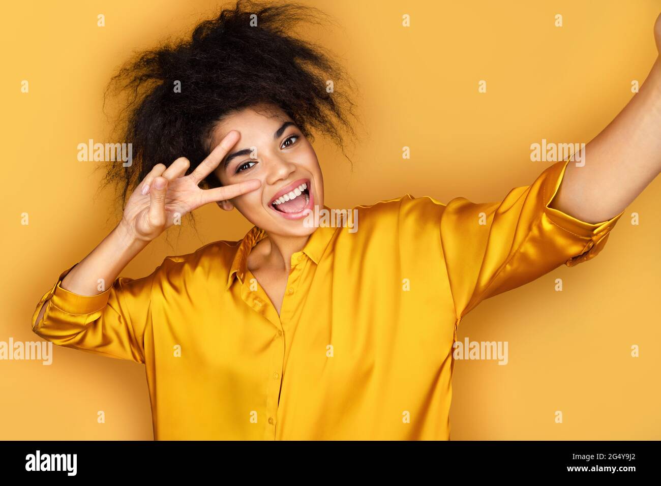 Une jeune fille gaie prenant le selfie au téléphone. Photo d'une fille afro-américaine sur fond jaune Banque D'Images