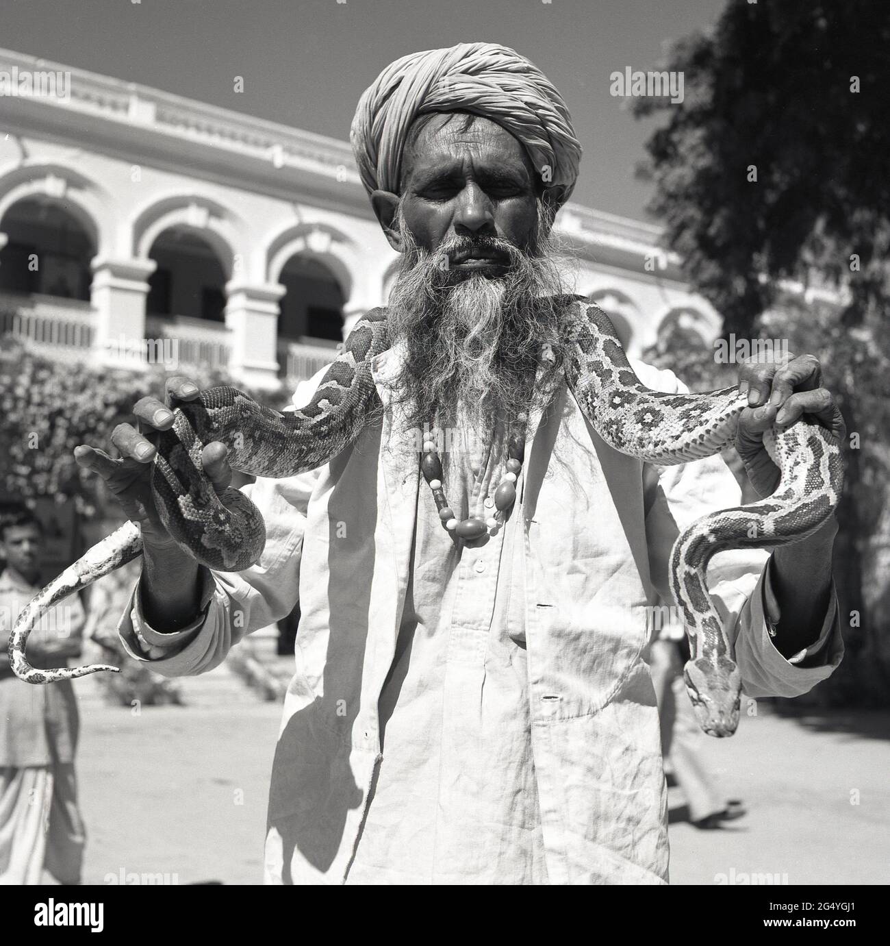 1950s, historique, debout pour son photon un indien avec une longue barbe et portant un turban, un charmeur de serpent, avec un serpent, un python, autour de son cou, Inde. Banque D'Images
