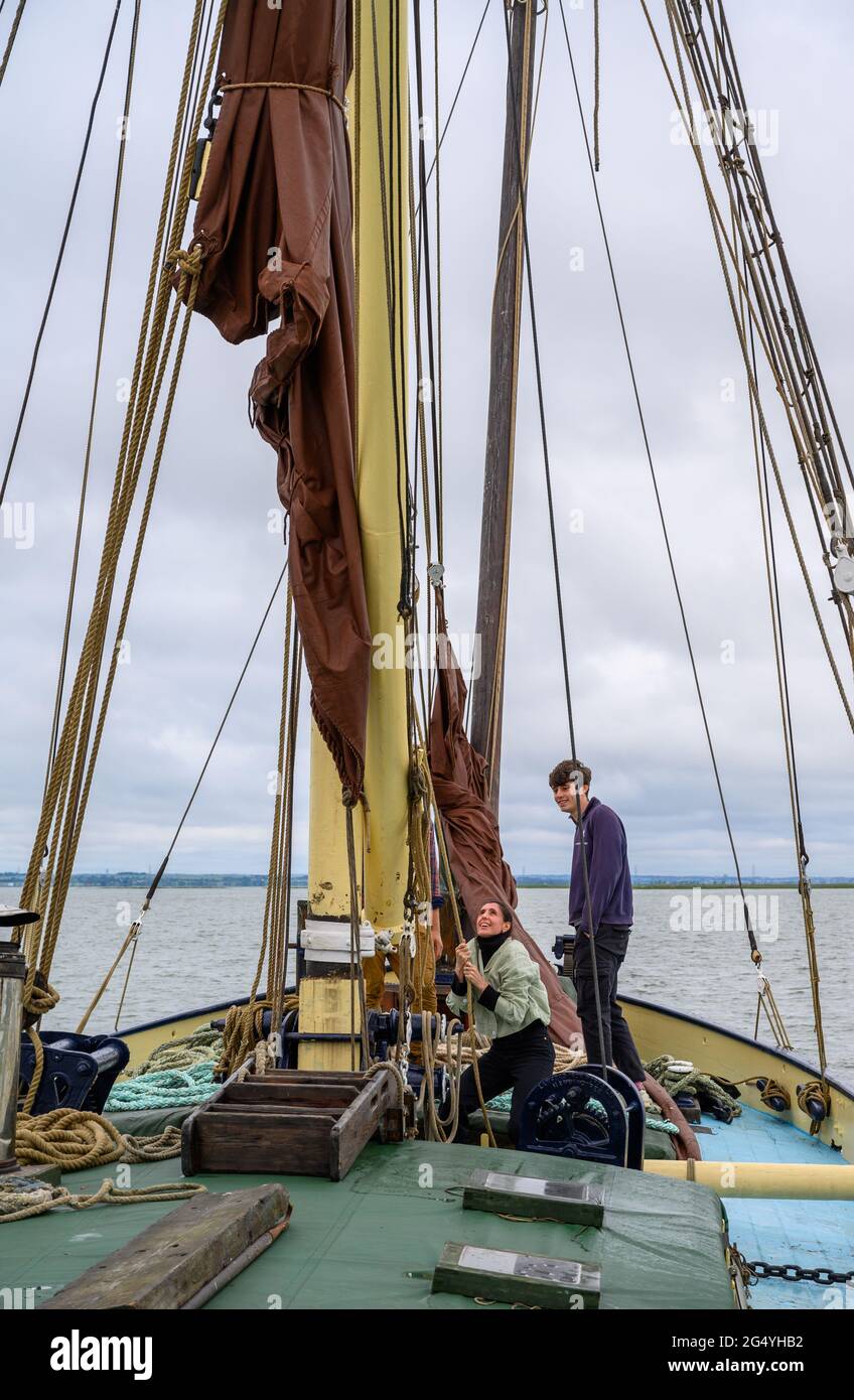 Apprendre les cordes: Deux passagers sur la barge 'Edith May' aidant le skipper Ed Gransden à lever une voile sur un voyage dans l'estuaire de la Tamise, Kent, Angleterre. Banque D'Images