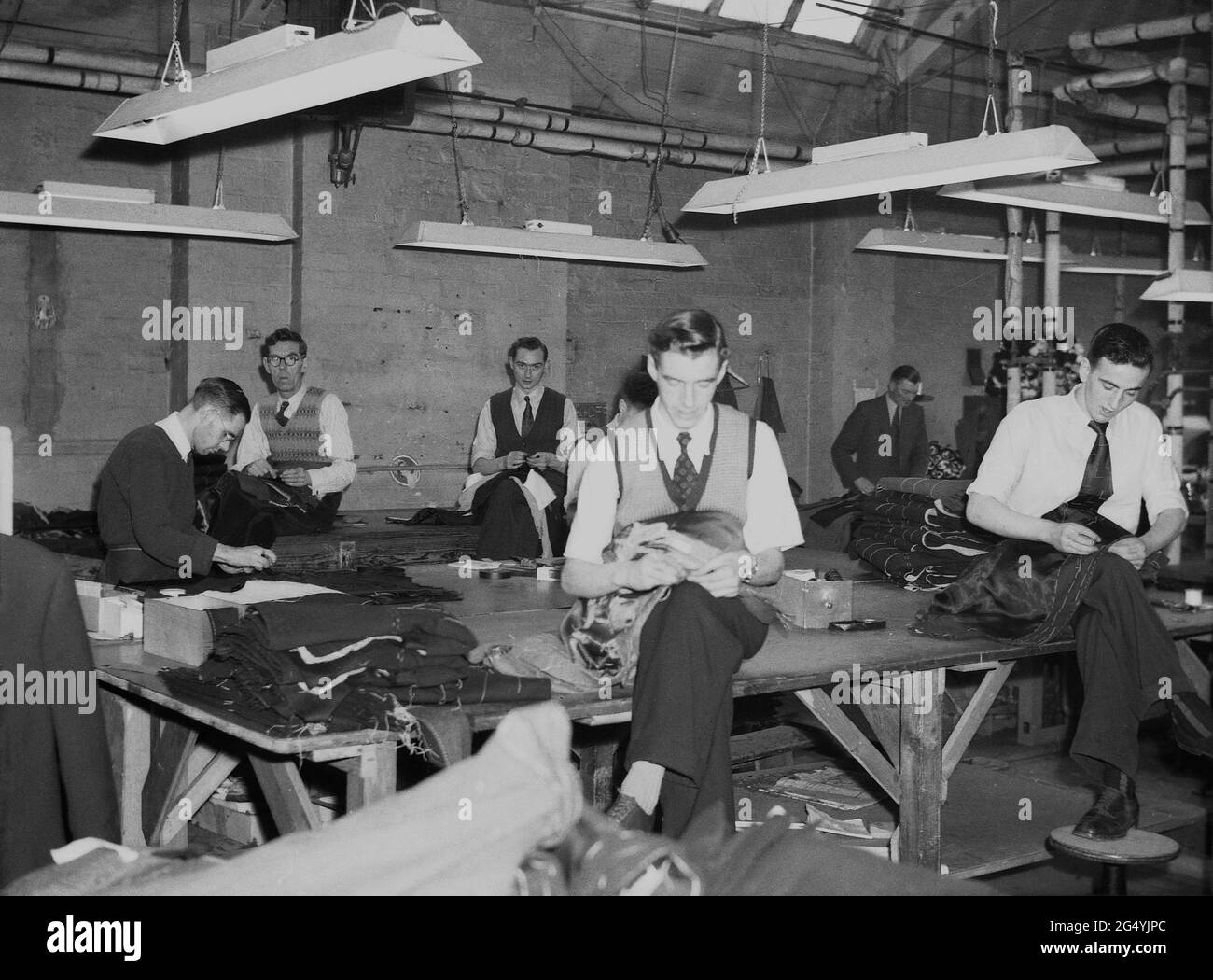 1957, tailleurs hommes historiques, assis sur des tables de chevalets au travail chez les fabricants de vêtements Joseph Hepworth & son, dans leur usine de Claypit Lane, Leeds, Angleterre, Royaume-Uni. En 1864, Joseph Hepworth est devenu un tailleur et un innovateur, comme en 1890s il avait établi 107 magasins pour vendre ses costumes et vêtements de gentlemen directement au public. En 1920s, Hepworths était devenu le plus grand fabricant de vêtements du Royaume-Uni et est maintenant connu sous le nom de Next PLC Banque D'Images