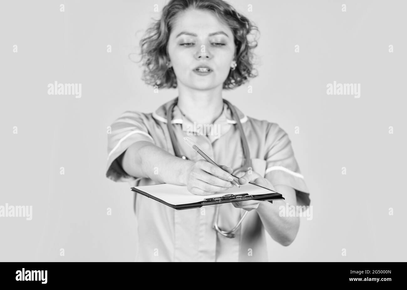 L'administration hospitalière féminine dans un centre médical moderne. L'infirmière en manteau médical avec des documents écrit des informations importantes. L'infirmière écrit des données Banque D'Images