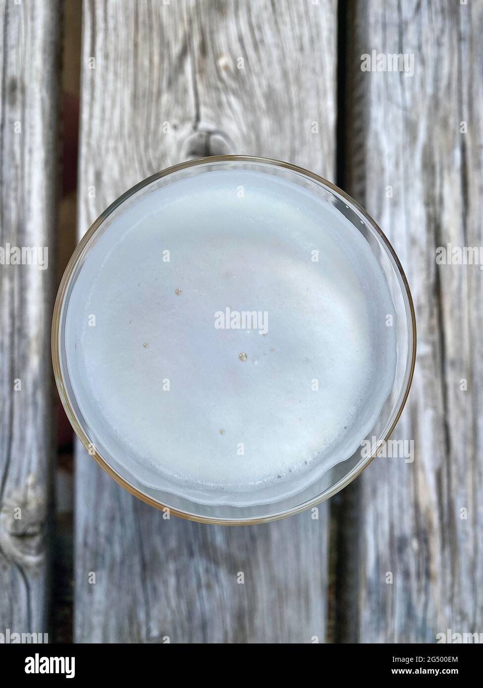 Un verre plat de bière vu d'en haut sur une table en bois dans le jardin de bière. En regardant vers le bas sur la mousse. Banque D'Images