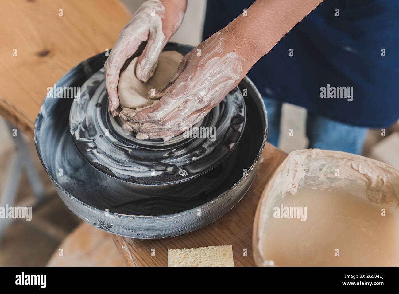 vue partielle de la jeune femme afro-américaine façonnant pot d'argile humide sur la roue près de l'éponge et de l'eau dans la boîte en plastique en poterie Banque D'Images