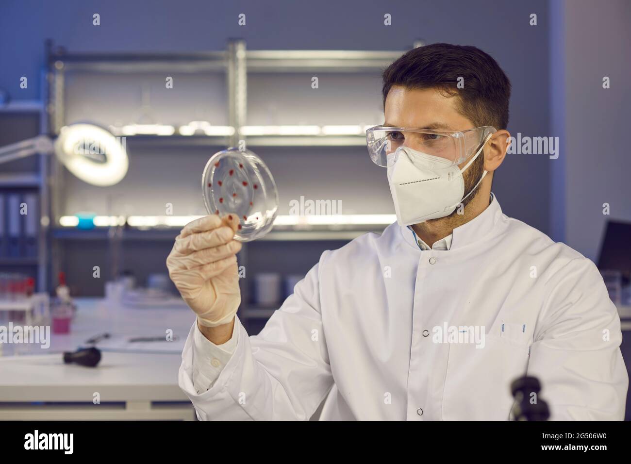Portrait d'un jeune homme scientifique dans un masque facial et des lunettes de protection tenant une boîte de Petri Banque D'Images