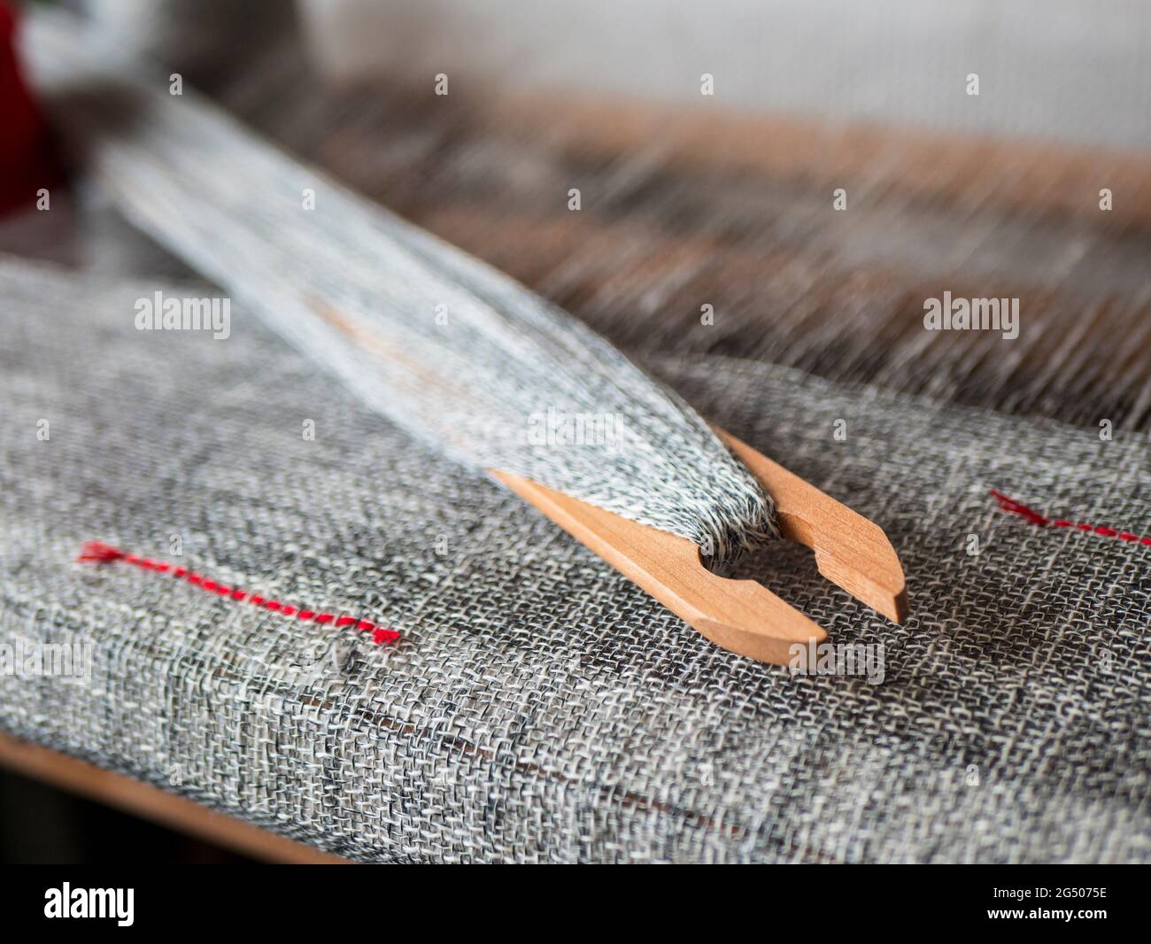 Une navette en bois avec du fil marbré est sur le métier à tisser à la main. Tissu gris tissé avec rayures rouges Banque D'Images