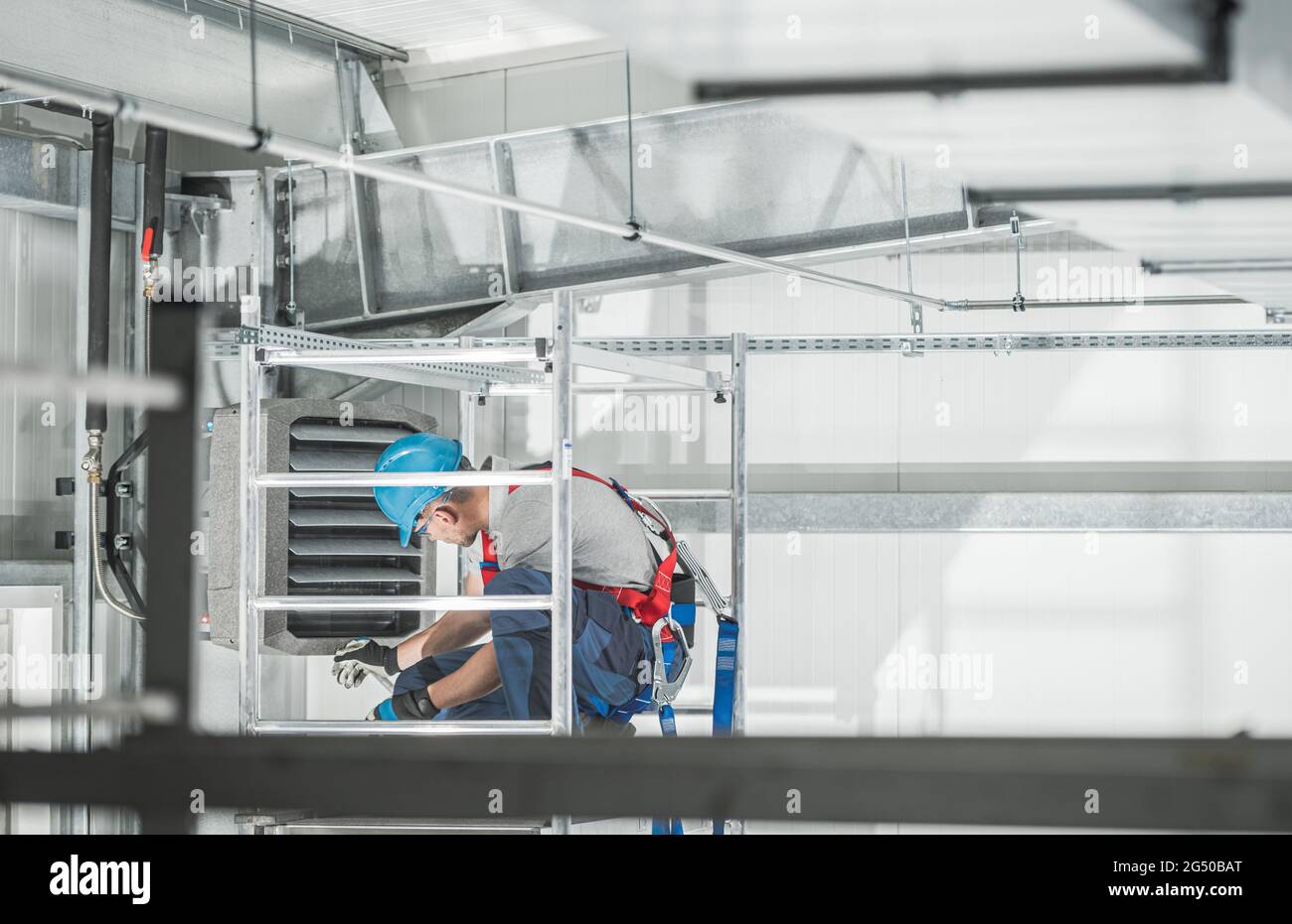 Vérification du faisceau de sécurité du travailleur du système CVC caucasien sur le système de chauffage de l'entrepôt commercial installé sur le mur du bâtiment. Banque D'Images