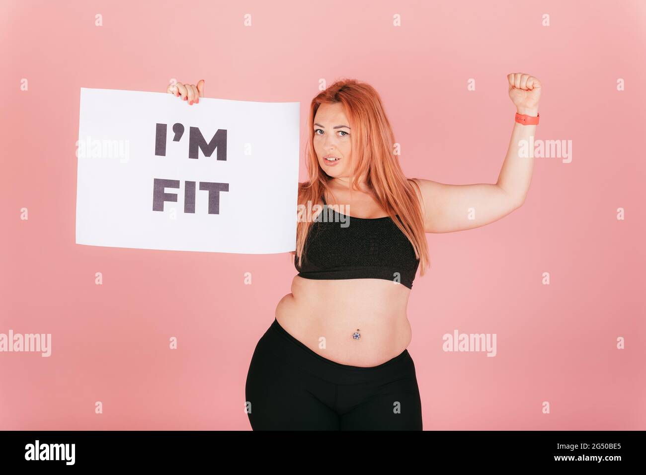 Belle femme forte avec corps de plus taille montrant l etiquette avec je suis en forme de texte et en tenant le poing vers le haut sur fond rose Photo Stock Alamy