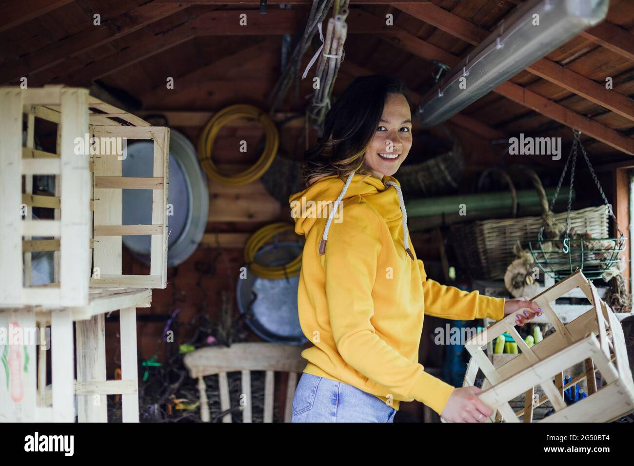 Une jeune femme debout dans un hangar regardant la caméra et tenant une caisse en bois. Elle organise le hangar. Banque D'Images