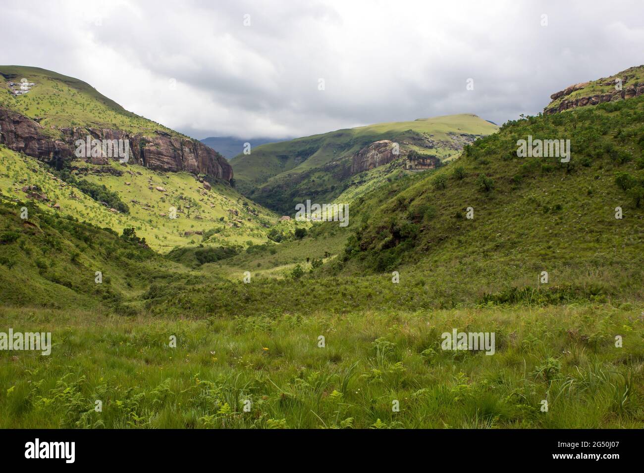 Une vallée entourée par les pentes couvertes d'herbe des montagnes du Drakensberg, en Afrique du Sud, avec des nuages de tempête se rassemblant au loin Banque D'Images