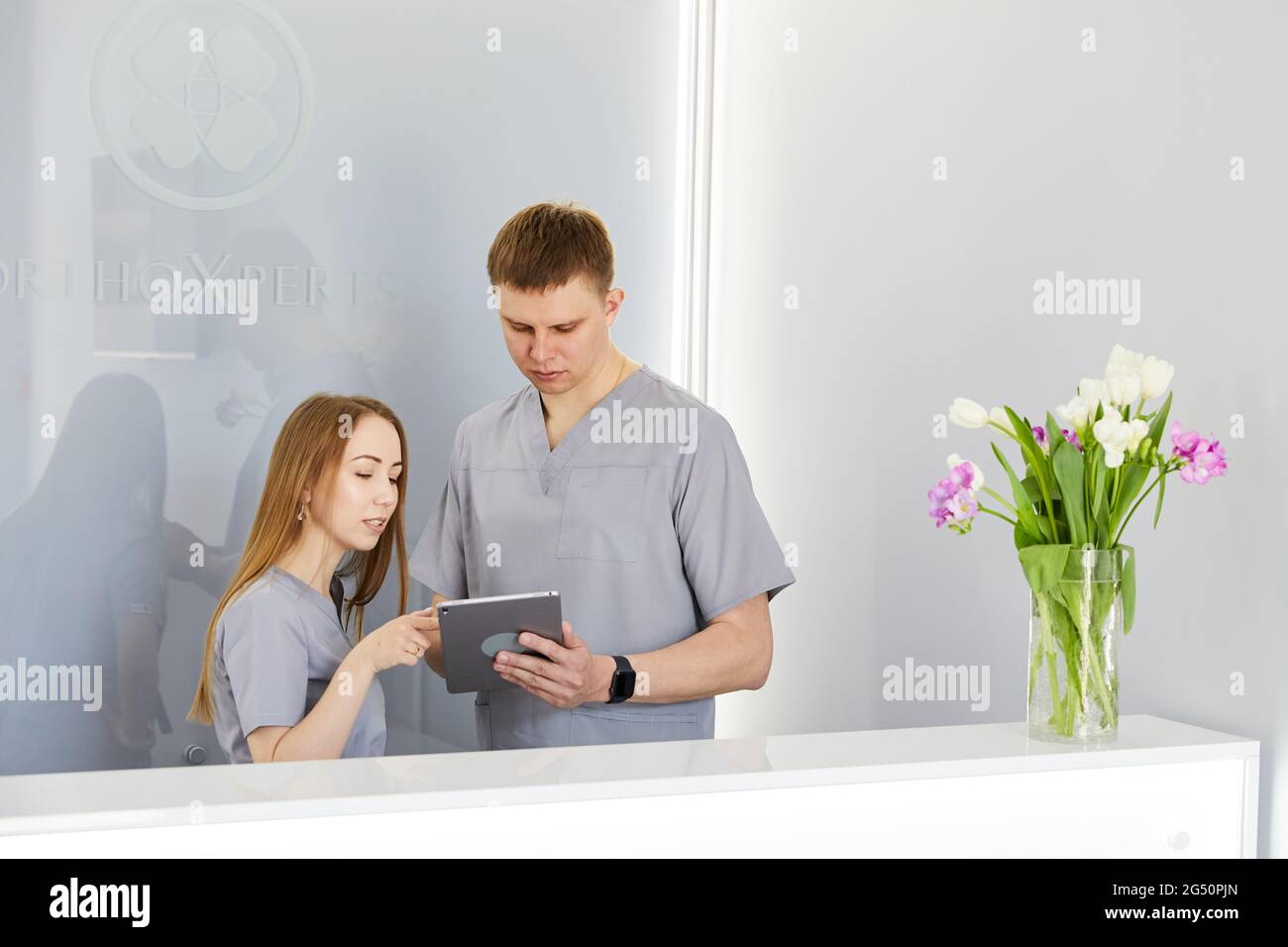 Dentiste avec infirmière dentaire dans un cabinet dentaire moderne utilisant un PC tablette portant l'uniforme. Spécialiste en orthodontie et assisant à la réception en clinique dentaire d Banque D'Images