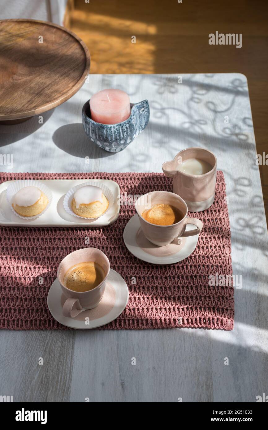 Petit déjeuner rose paisible pour deux servi sur une nappe rose avec deux tasses de café, un goûter avec deux gâteaux au citron et un pot de lait sur une table en bois. Banque D'Images
