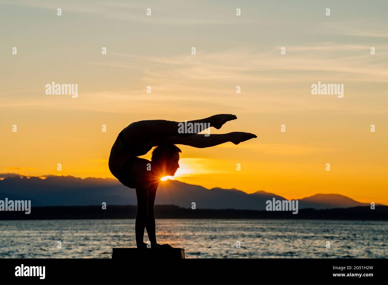 Silhouette de femme faisant une posture acrobatique se pose contre la mer au coucher du soleil Banque D'Images