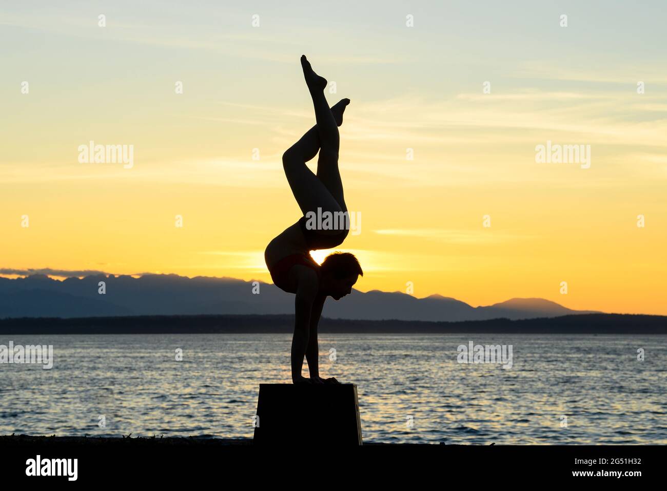 Silhouette de femme faisant une posture acrobatique se pose contre la mer au coucher du soleil Banque D'Images