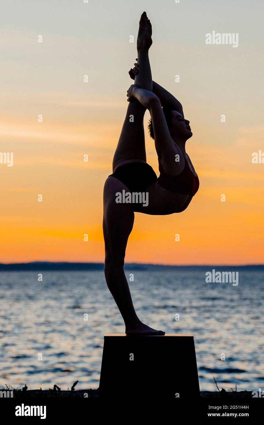 Silhouette de femme faisant une posture acrobatique contre la mer au coucher du soleil Banque D'Images