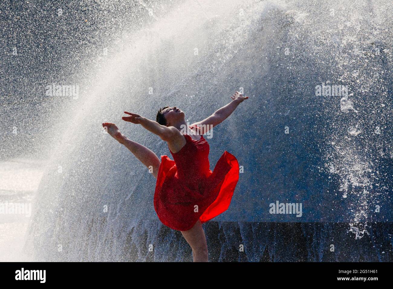 Femme en robe rouge dansant contre la fontaine Banque D'Images