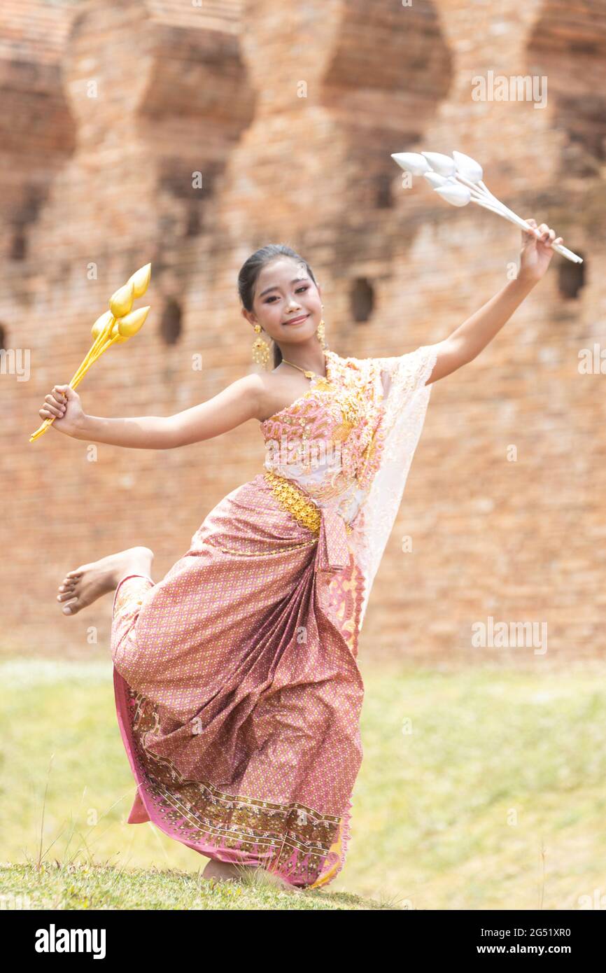 Une écolière asiatique aux cheveux longs vêtue de costumes traditionnels thaïlandais contient des fleurs argentées et dorées et exécute des mouvements de danse. Banque D'Images