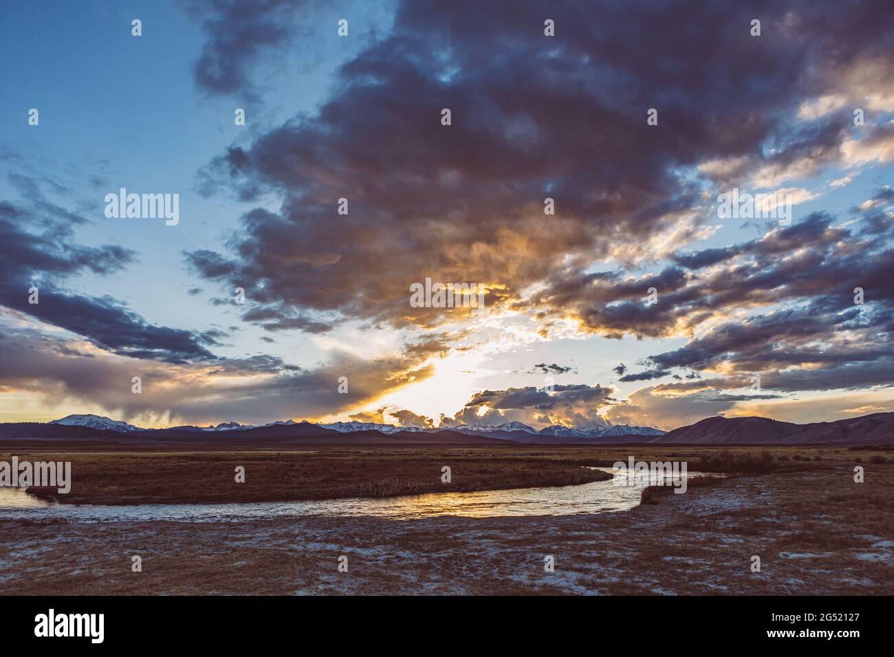 La rivière s'étend sur une plaine aride, au coucher du soleil et dans les montagnes Banque D'Images