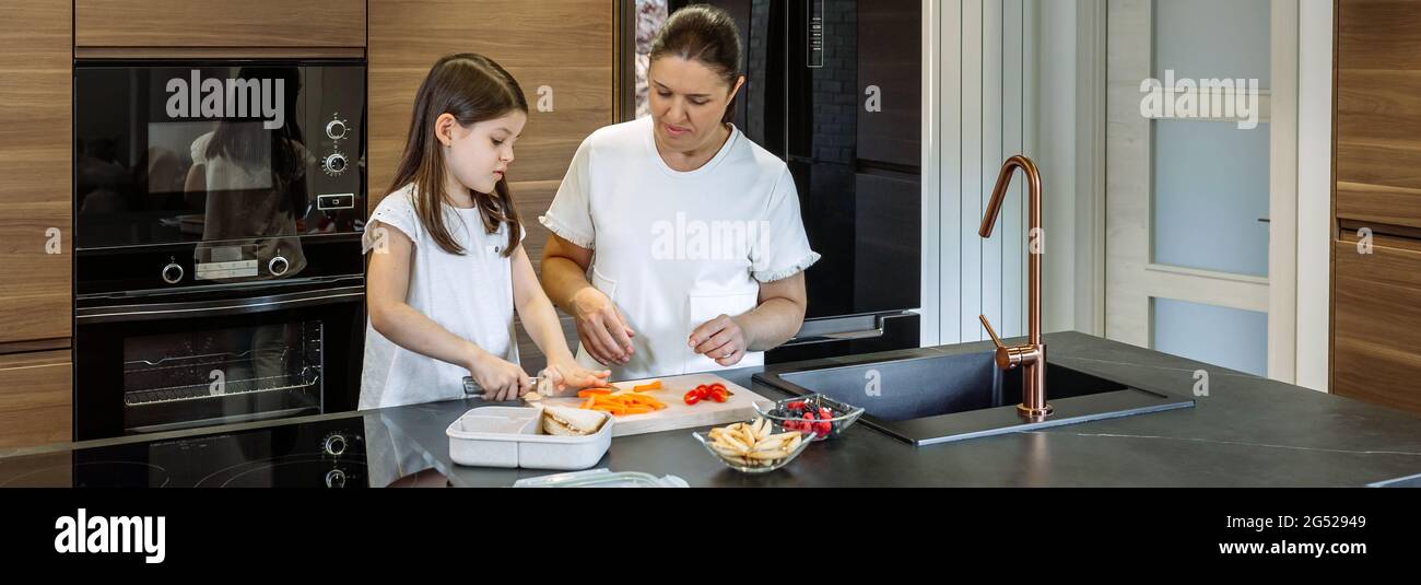 Mère enseignant à sa fille de couper des légumes pour la boîte à lunch Banque D'Images