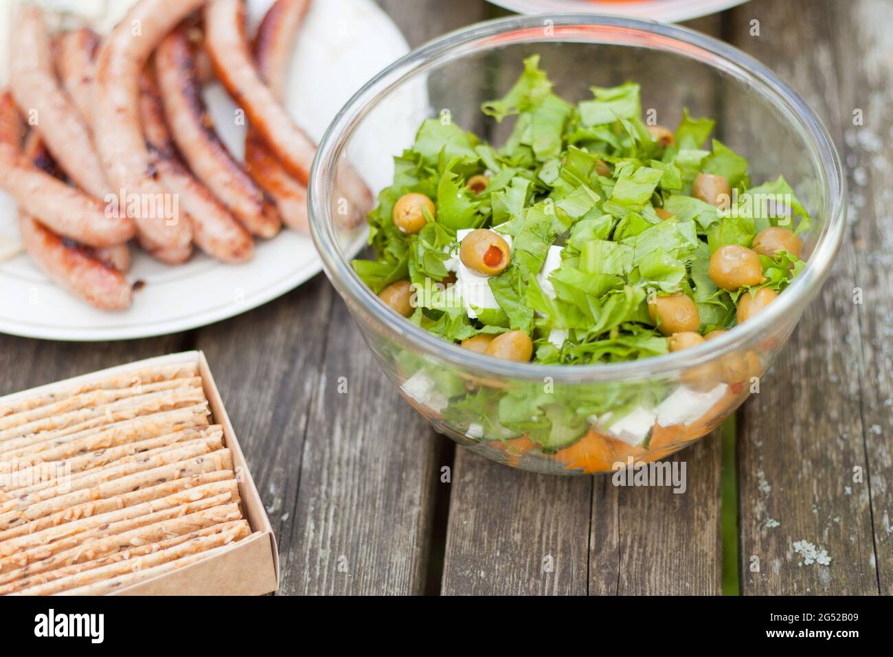 Salade fraîche et saine avec olives et chas de feta sur une table en bois. Croustilles cuites au four avec des saucisses au moment du pique-nique. Plats frais et savoureux Banque D'Images