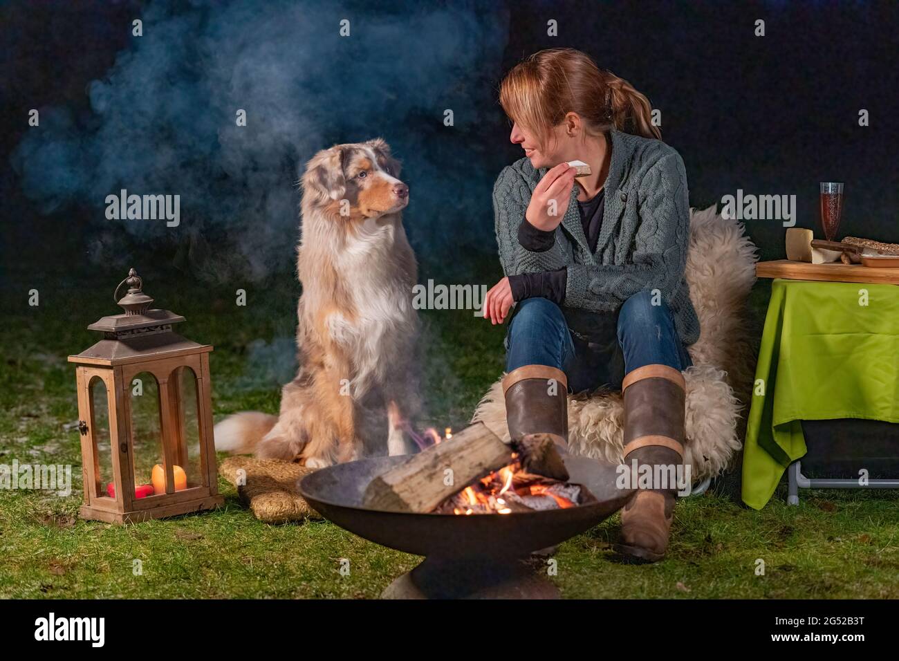 La jeune femme mange une tranche de baguette avec brie. Son jeune Berger australien est assis à côté d'elle, regardant le petit pain avec ses yeux bleus. Banque D'Images