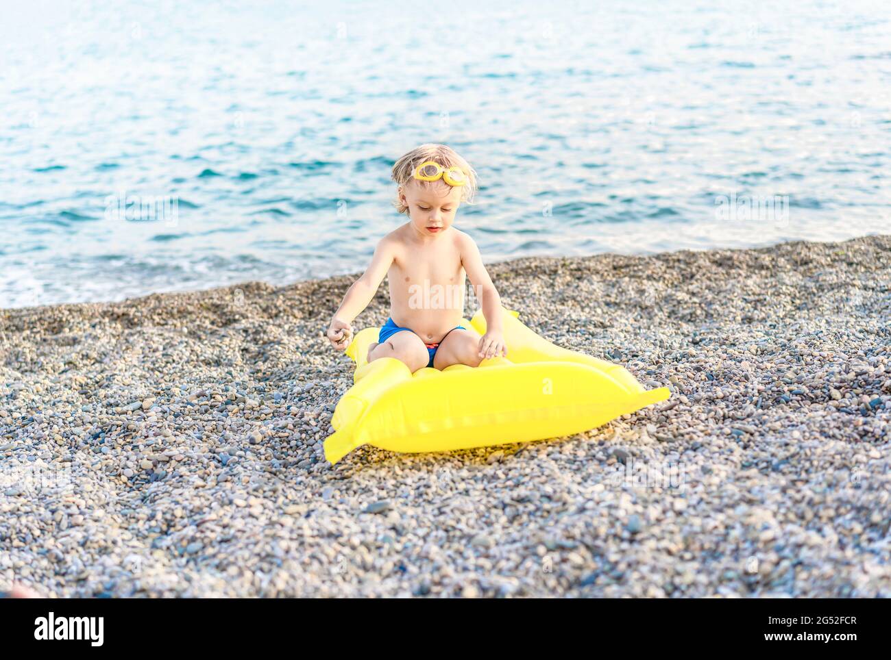 Mignon drôle petit garçon jouant avec matelas jaune de natation au bord de mer. Vacances d'été à la plage, style de vie d'enfance, voyage de vacances, concept de scène de plage. Banque D'Images