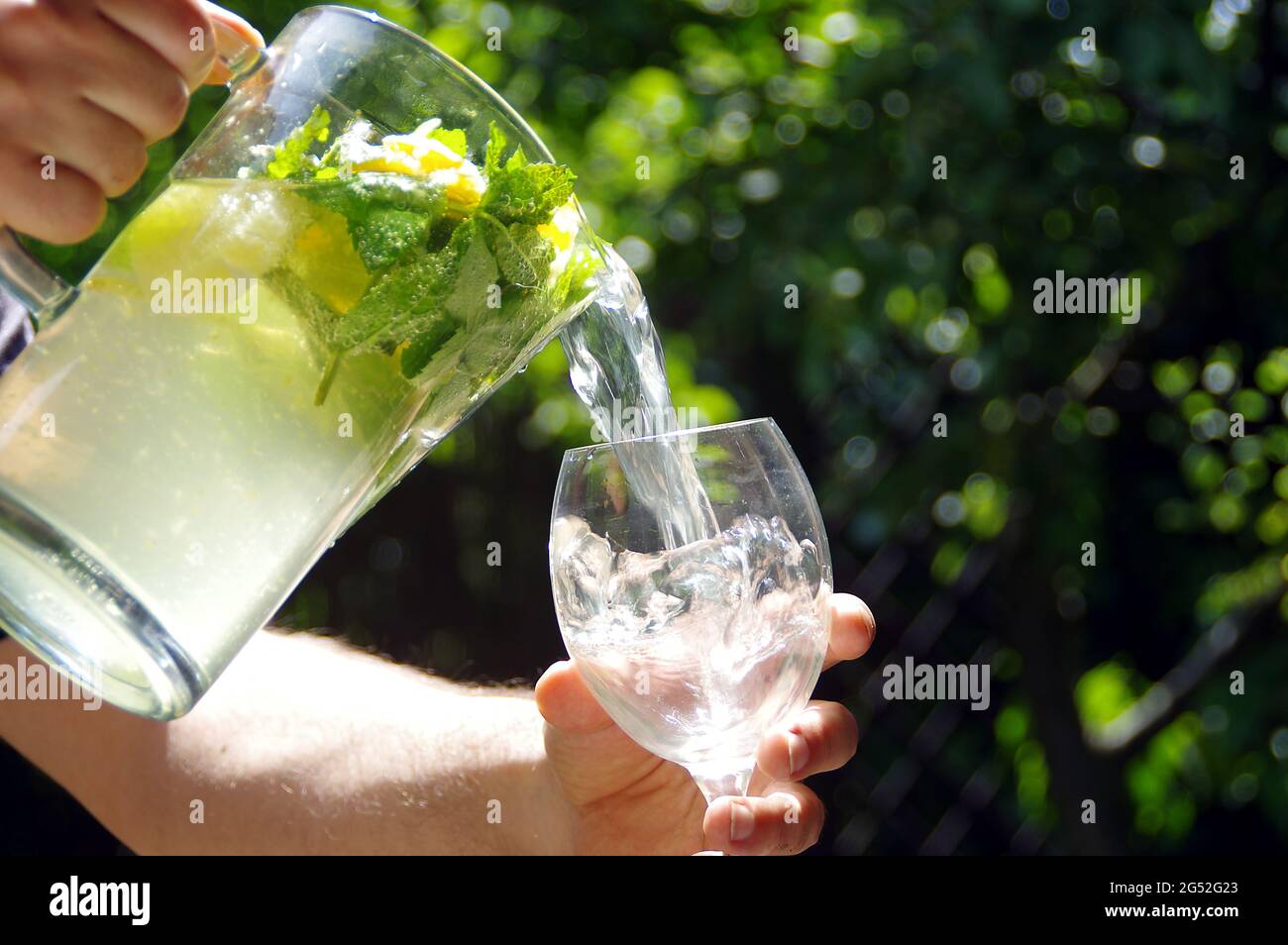 Une boisson froide au citron avec des tranches d'agrumes versées dans un verre à partir d'une carafe. Limonade maison fraîche et fraîche. Boisson à la menthe biologique avec eau. Banque D'Images