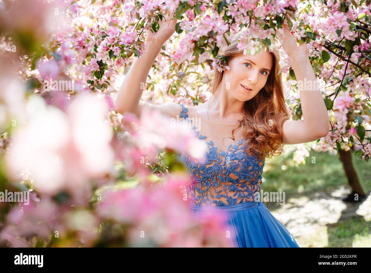 Femme aux cheveux rouges sur fond de fleurs roses. Banque D'Images