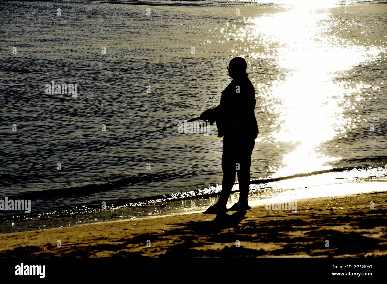 HOMME PÊCHE DEPUIS LA PLAGE AU COUCHER DU SOLEIL Banque D'Images