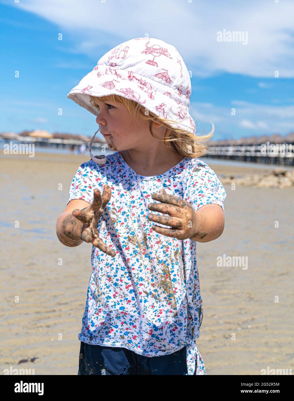 Petite fille caucasienne portant un chapeau jouant sur la plage montre ses  mains boueuses Photo Stock - Alamy