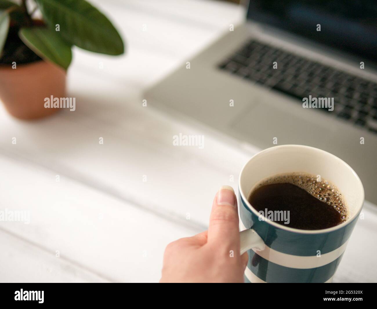 La grande tasse de café dans la main près de l'ordinateur portable Banque D'Images