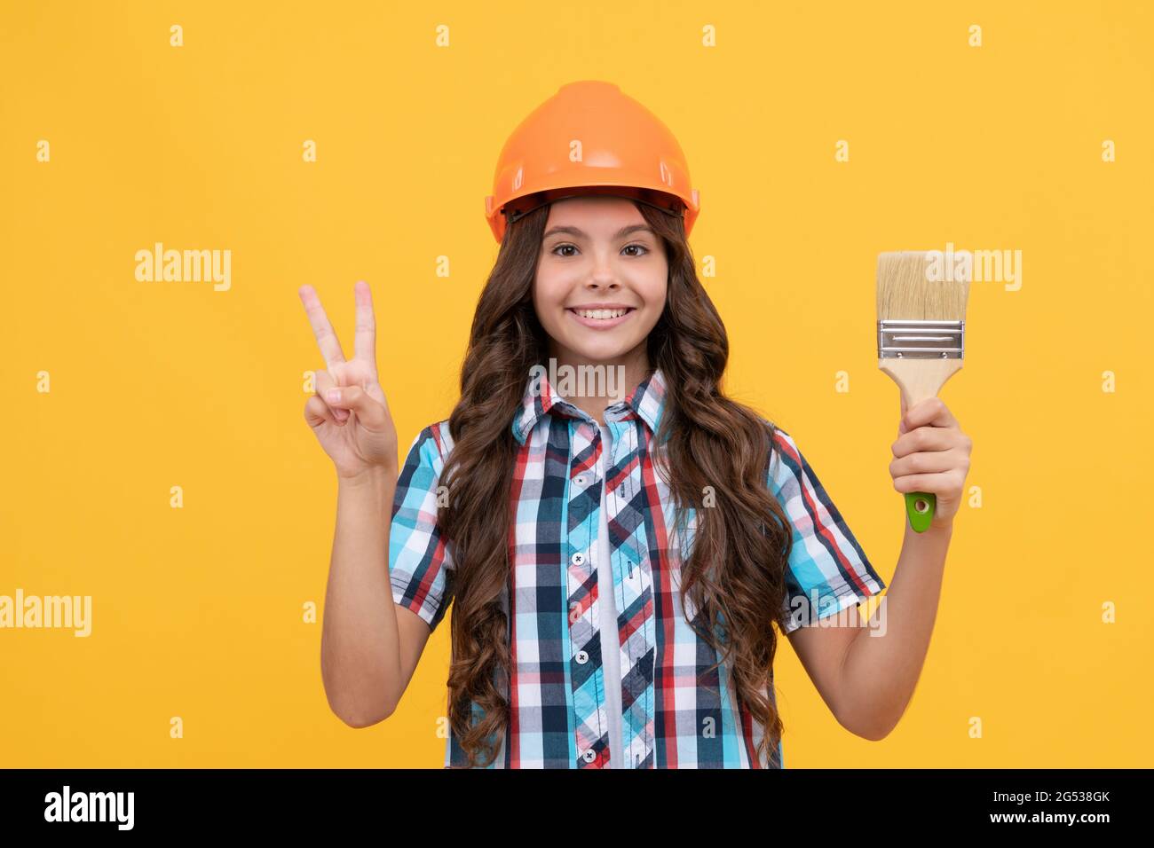 bonne adolescente dans la construction casque tenir la peinture brosse montrer la paix geste, la décoration. Banque D'Images